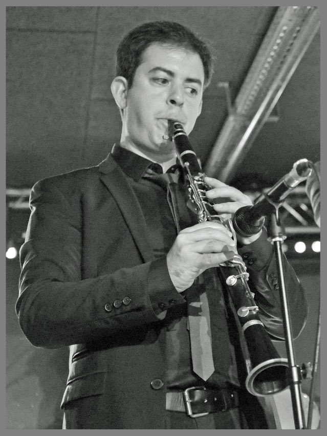 Photo noir et blanc du clarinettiste Sylvain Hamel jouant en costume cravate devant un micro.